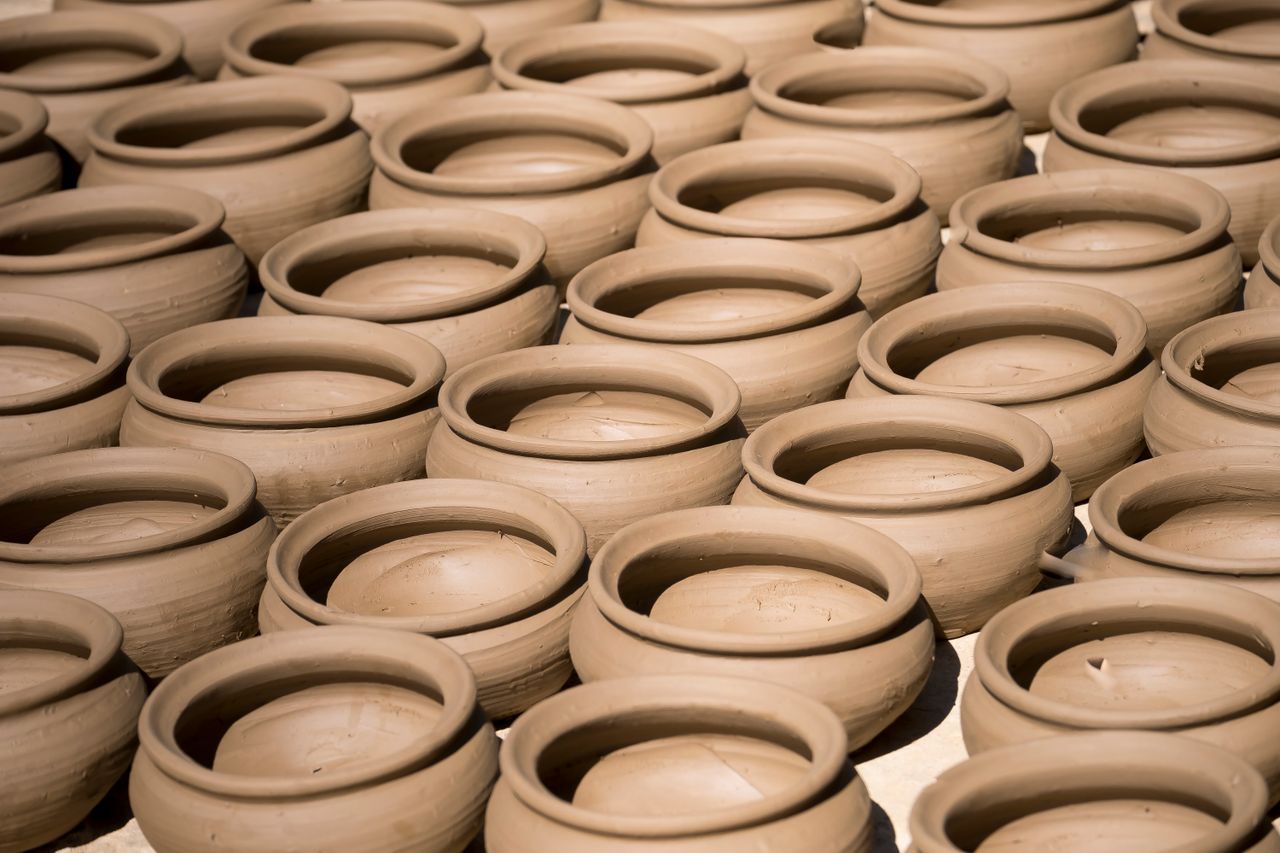 Rows of unfinished handmade clay pots drying in the sunlight, showcasing traditional pottery.