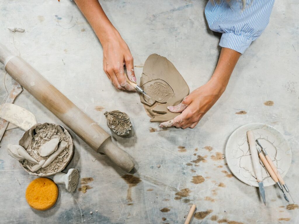 Hands crafting ceramic pieces with tools in a pottery workshop, showcasing creativity and skill.